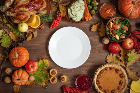 感恩节晚餐背景与火鸡和各面菜南瓜派落叶和季节性秋季装饰围绕白色盘子顶部视图复制空间。