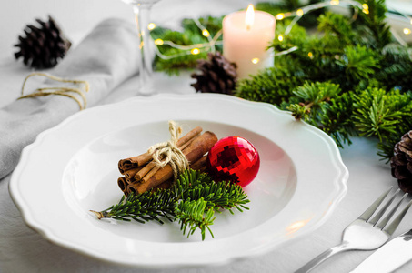 节日圣诞节和新年餐桌设置斯堪的纳维亚风格的自然和白色色调。 用绿色杉树枝蜡烛松果和肉桂棒装饰的餐厅。