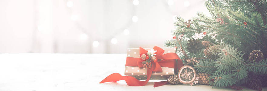 圣诞节舒适在一个房间的灯光背景上，有一棵圣诞树的灯光和树枝，桌子上有一个红色蝴蝶结的礼物，供文字使用