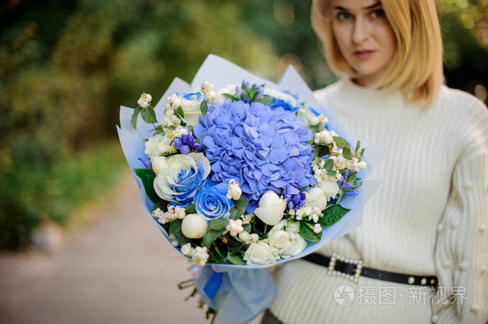 金发碧眼的女孩穿着白色的汗衫手里拿着一束蓝色的小花
