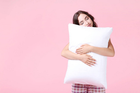美丽的女孩抱着粉红色背景的白色枕头