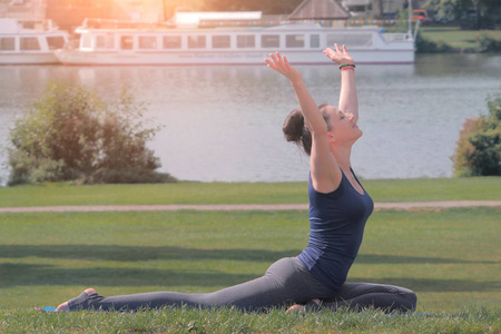 妇女练习瑜伽和提高她的手在公园在绿色草地上