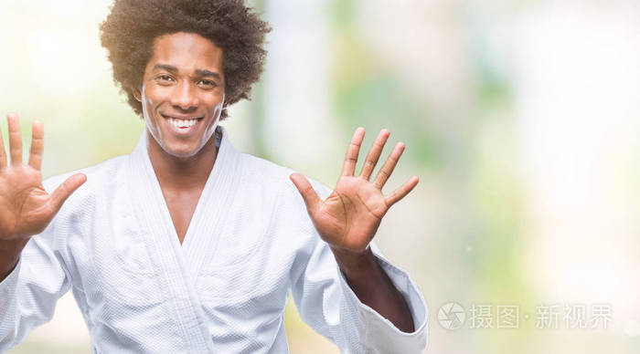 美国黑人男子穿着空手道和服，在孤立的背景下，显示和指着10号手指，同时微笑自信和快乐。