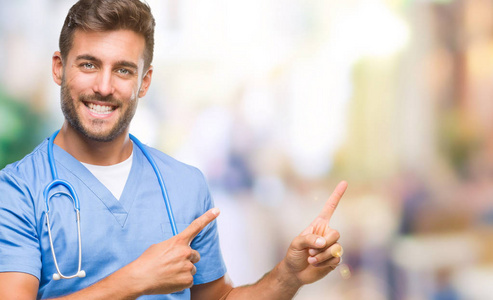 年轻英俊的医生外科医生，男人在孤立的背景上微笑，看着相机，用两只手和手指指向一边。