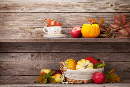 秋天的静物卡片，用南瓜苹果梨咖啡杯和五颜六色的叶子放在木墙前。 与您的文本空间