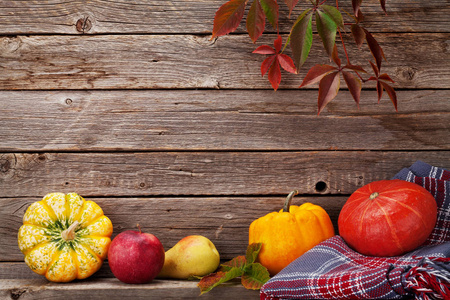 秋天的静物卡片，用南瓜苹果梨和五颜六色的叶子放在木墙前。 与您的文本空间