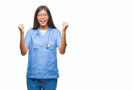 年轻的亚洲医生女人在孤立的背景下庆祝惊讶和惊讶的成功，举起手臂和睁开眼睛。 赢家概念。
