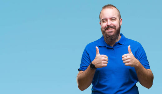 年轻的白种人臀部男子穿着蓝色衬衫,在孤立的背景上,成功标志,做积极