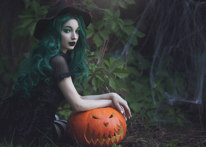 漂亮南瓜万圣节女巫,绿色的头发,拿着一个雕刻的可怕的南瓜.