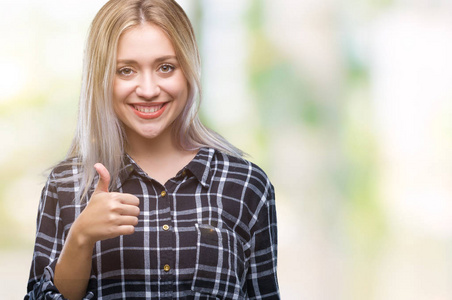 年轻的金发女人在孤立的背景下，用手做快乐的竖起大拇指的手势。 赞许的表情看着相机，显示出成功。