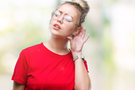 年轻的金发女人戴着眼镜，在孤立的背景上微笑，用手捂住耳朵听谣言或流言蜚语。 耳聋概念。