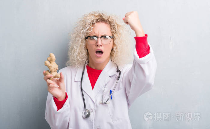 年轻的金发营养师女医生在灰墙上抱着姜生气和沮丧愤怒疯狂地大喊大叫