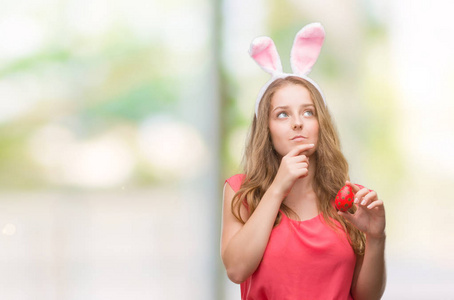年轻的金发女人戴着复活节兔子耳朵，严肃的脸，思考问题，想法