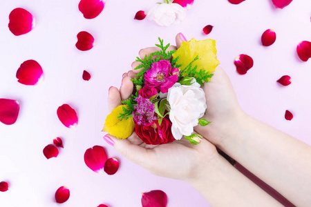 美丽温柔的手，粉红色的背景手上有花和花瓣，美丽明亮的妆容和玫瑰花瓣