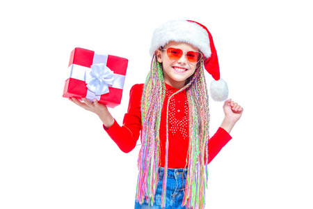 女孩在圣诞老人帽子。小可爱女孩的肖像抱着圣诞礼物的盒子, 小女孩抱着她的礼物与快乐和有趣的表达孤立在白色背景。节日礼品