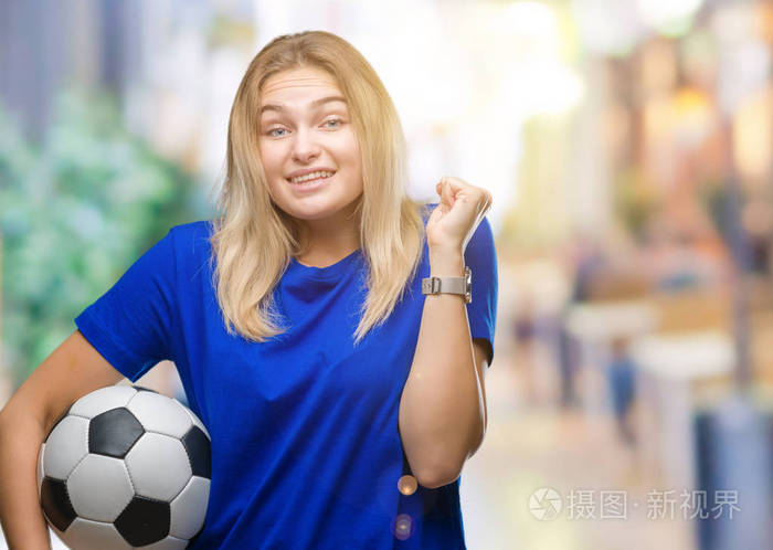 年轻的白种人女子抱着足球在孤立的背景下尖叫自豪和庆祝胜利和成功