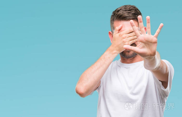 年轻的帅哥在孤立的背景上用手遮住眼睛,用悲伤和恐惧的表情做停止的