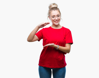 年轻的金发女人戴着眼镜在孤立的背景上做手势，双手显示大尺寸的标志符号。 微笑着看着相机。 测量概念。