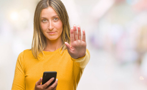 年轻漂亮的女人用智能手机在孤立的背景下发送信息，张开手做停止标志，严肃自信的表情防御手势