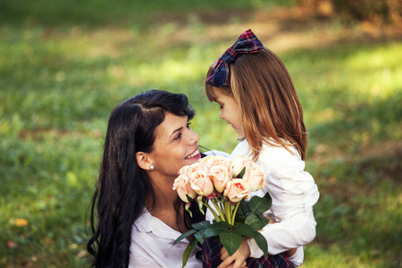 年轻的母亲和女儿在一个美丽的秋天一起在户外享受。 他们很高兴。 一个小女孩想给她妈妈一束漂亮的花