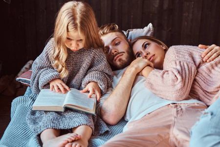 妈妈, 爸爸和女儿躺在床上一起读故事书
