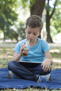 学龄前的小可爱男孩坐在草地上时使用数字平板电脑。 他看着他最喜欢的视频剪辑。 下一代数字