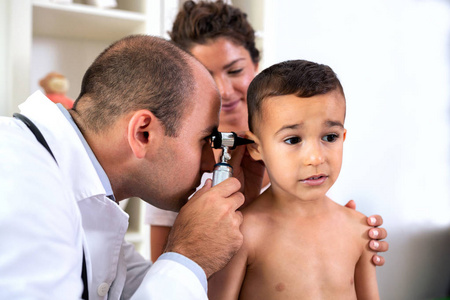 儿童专科医生在母亲手中的一个年轻病人的耳朵里看