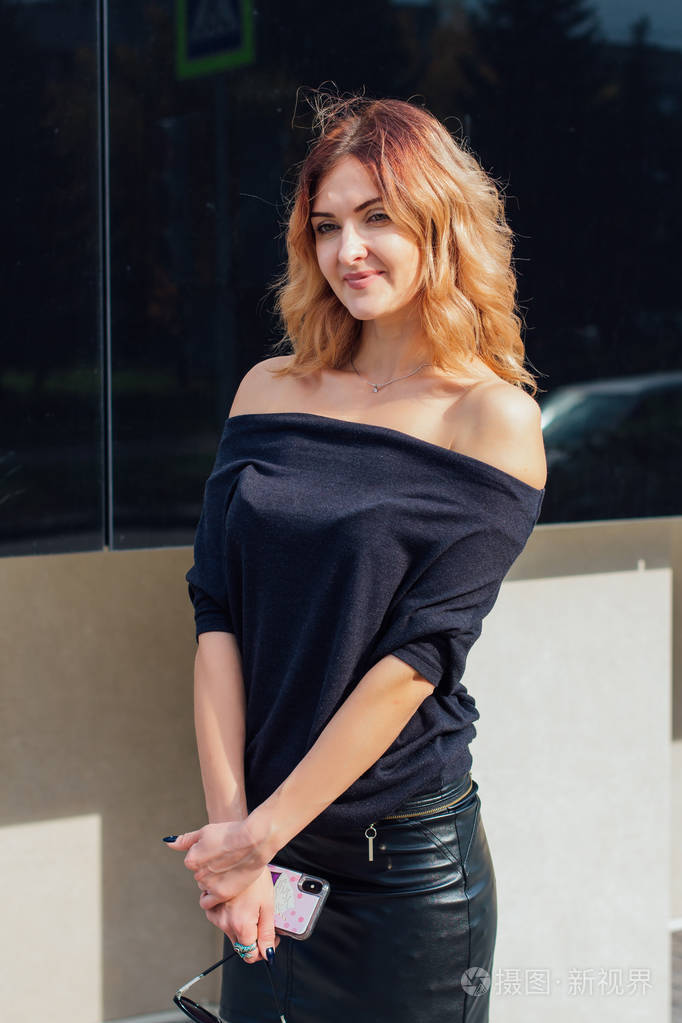 一位穿着黑色连衣裙的迷人女子的肖像肩膀敞开站在现代建筑旁边