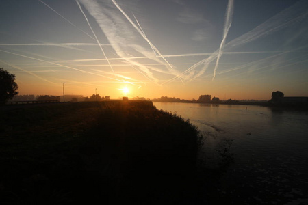 日出与彩色飞机跟踪雾在草地和堤坝在荷兰霍兰切伊塞尔河在尼厄沃尔克。