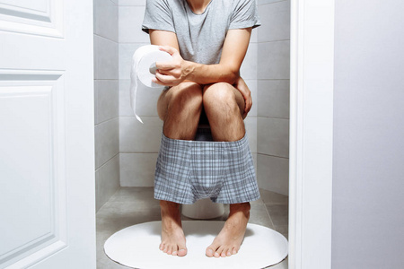 男人坐在马桶上拿着纸巾-健康问题的概念.照片