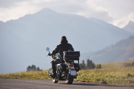 黑色皮夹克骑摩托车骑摩托车在模糊的复制空间背景下，美丽的雾木本山脉和蓝色多云的天空在阳光明媚的夏天。