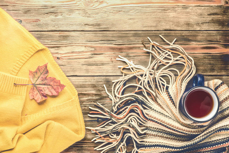 秋季时尚的季节性概念，黄色温暖柔软舒适的毛衣开衫斯堪的纳维亚针织围巾杯热红茶咖啡落下来的枫叶木桌平躺俯视复古