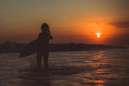 冲浪的女人带着冲浪板在海水中享受日落