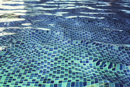 一种鱼眼效应，室内游泳池在蓝色瓷砖地板上荡漾着水。游泳池用瓷砖地板擦拭干净的水。浅水池中水的摆动。水下马赛克瓷砖。