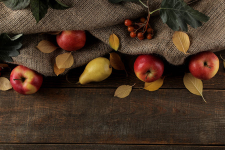 秋天的安排与水果，苹果，梨和黄色的秋叶在棕色的木桌上，有一个地方铭文。 顶部视图