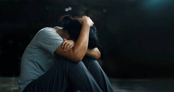 创伤后应激障碍. 沮丧的女人独自坐在地板上,在黑暗的房间背景下.