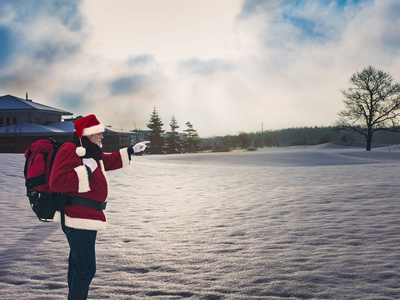 运动的圣诞老人带着背包站在白雪覆盖的田野上，用手指指向地平线。 积极健康的生活方式和旅游理念。