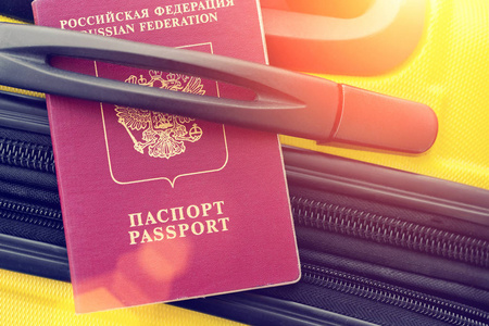 俄罗斯护照在阳光下黄色手提箱的手柄下。 色调