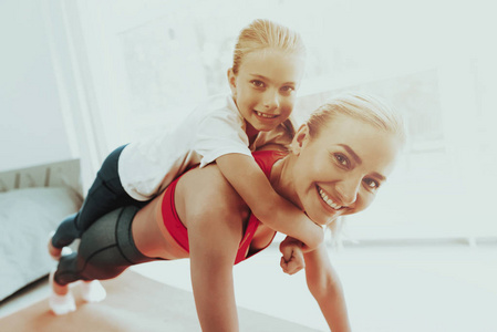 女人做俯卧撑，女儿在背上。 积极的生活方式。 一起放松。 在家健身。 假日休闲。 身体平衡。 体育锻炼。 躺在健身房的地毯上。 