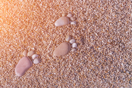 在阳光下用鹅卵石在沙子上留下的脚印. 色调照片