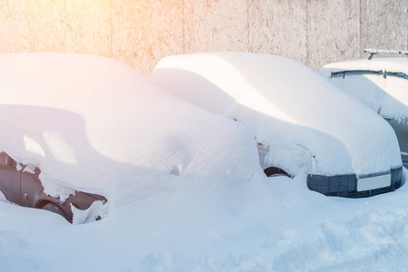 一排停着的车在阳光下覆盖着雪