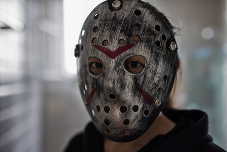 亚洲女人带着杰森面具和黑色连帽衫连衣裙,从窗户照下来.