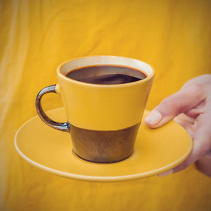 穿黄色衣服的女人拿着黄色和棕色的杯子和咖啡