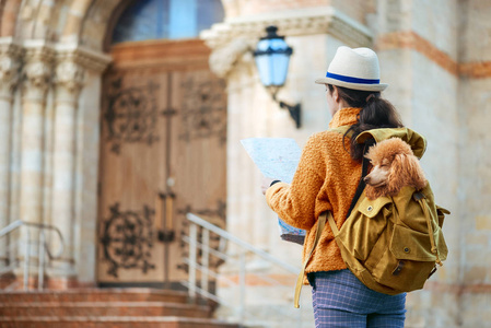 女旅行者带着狗在背包里检查建筑纪念碑。 旅行的概念。