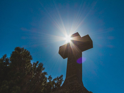 太阳升基督教符号石十字在深蓝色的天空背景上,从陆地上看到太阳.照片