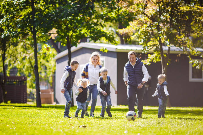 主题家庭户外活动。 一个友好的高加索家庭，六个爸爸妈妈和四个孩子在阳光明媚的日子里，在房子附近的草坪上，带着球跑着。