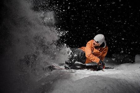 穿着橙色夹克的滑雪者在黑黑的夜晚骑在雪粉山上