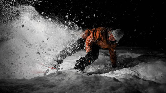 身穿橙色夹克衫的滑雪者在黑黑的夜晚骑在雪粉山上