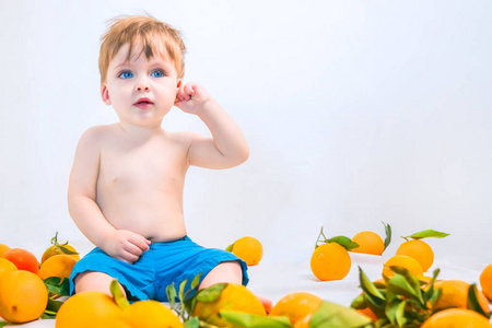 蓝色眼睛的金发小男孩穿着蓝色短裤坐在橘子周围
