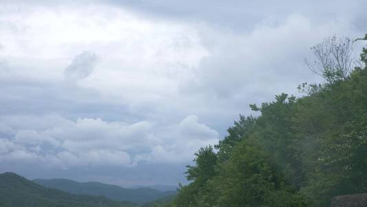 在多云的夏日里，从车窗看到一片山地景观，积云和树木